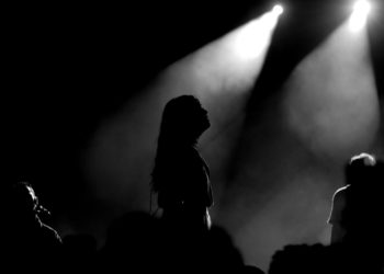 Silhouetted performers create a moody atmosphere under bright stage lights.
