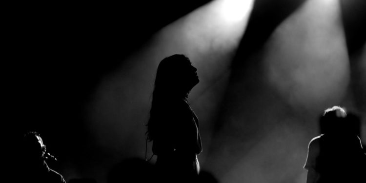 Silhouetted performers create a moody atmosphere under bright stage lights.